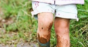 Pernas de criança usando botas e pisando na lama