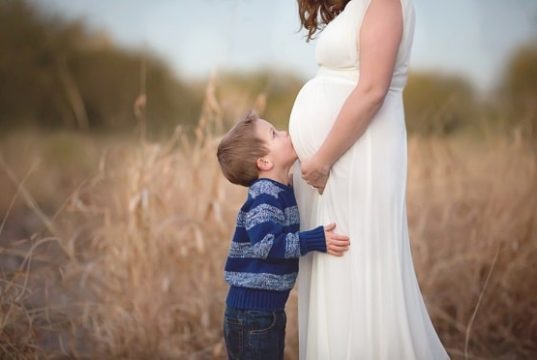 Menino bejando barriga de grávida de sua mãe